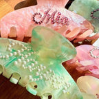 Pastel acrylic hair claws with pearl beads and rhinestone lettering details.