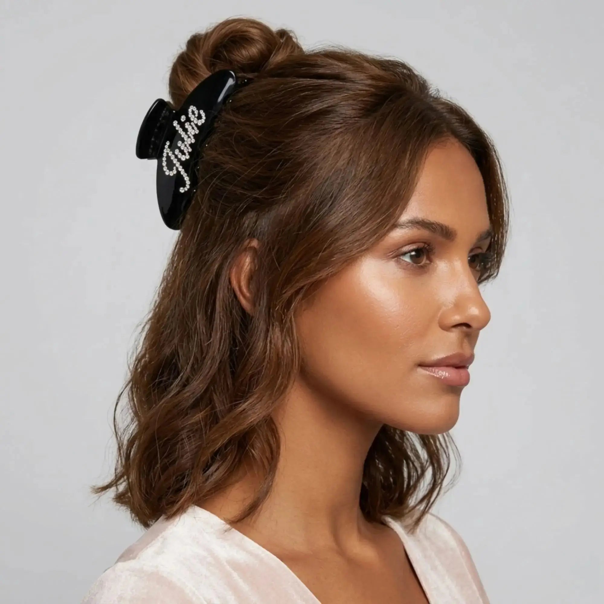 Black acetate hair claw with rhinestone lettering, clipped in styled hair.